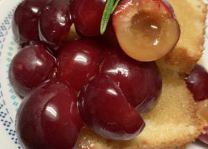 Halved bubblegum plums covered in honey sauce, served over vanilla pound cake on a decorative plate.