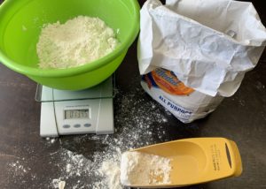 a kitchen scale, GOld Medal all-purpose flour, and measuring cup on a dark table